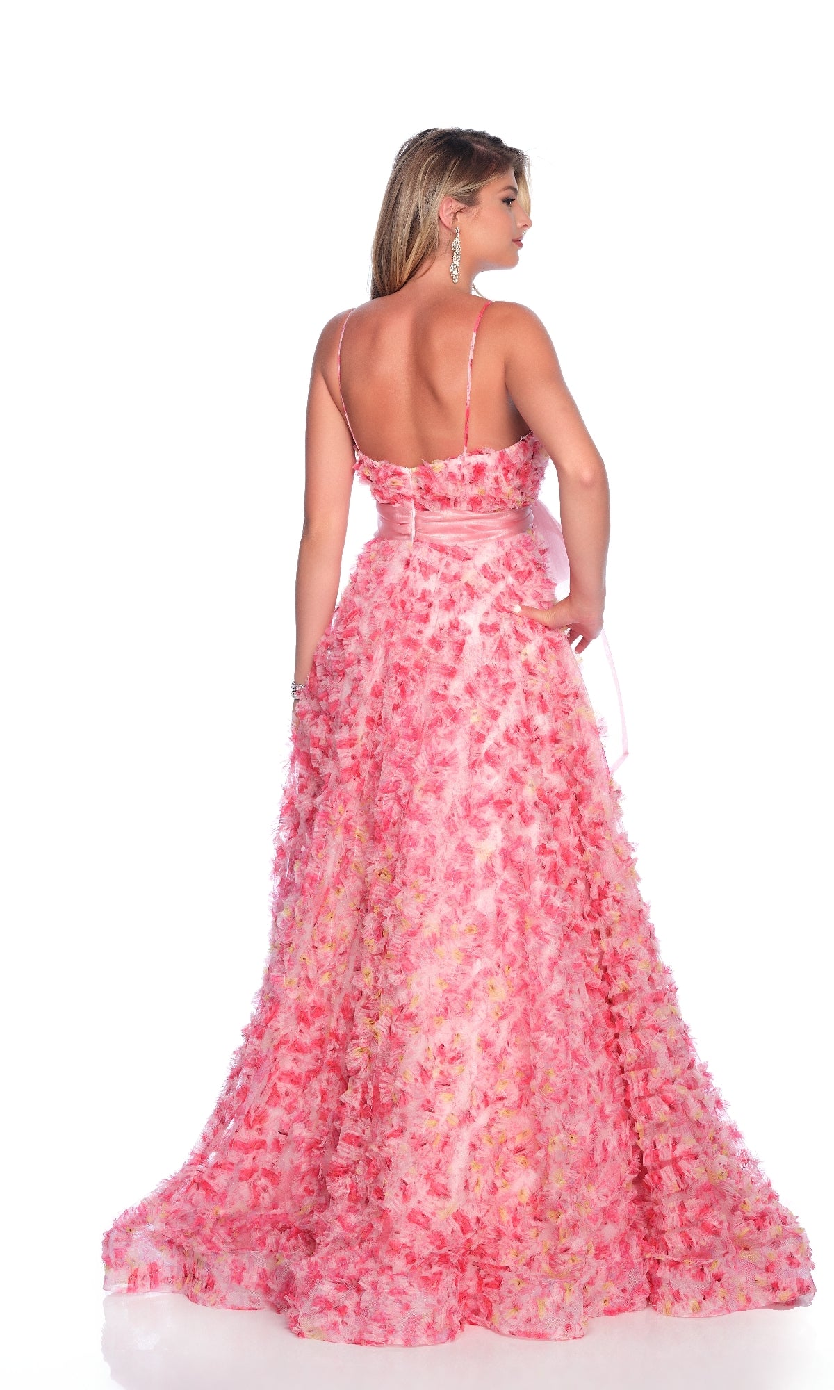 A woman stands with her back to the camera in the Dave & Johnny 12136 Pink Print Bow Prom Ball Gown, featuring thin straps, a full skirt, and an oversized bow, set against a plain white background.